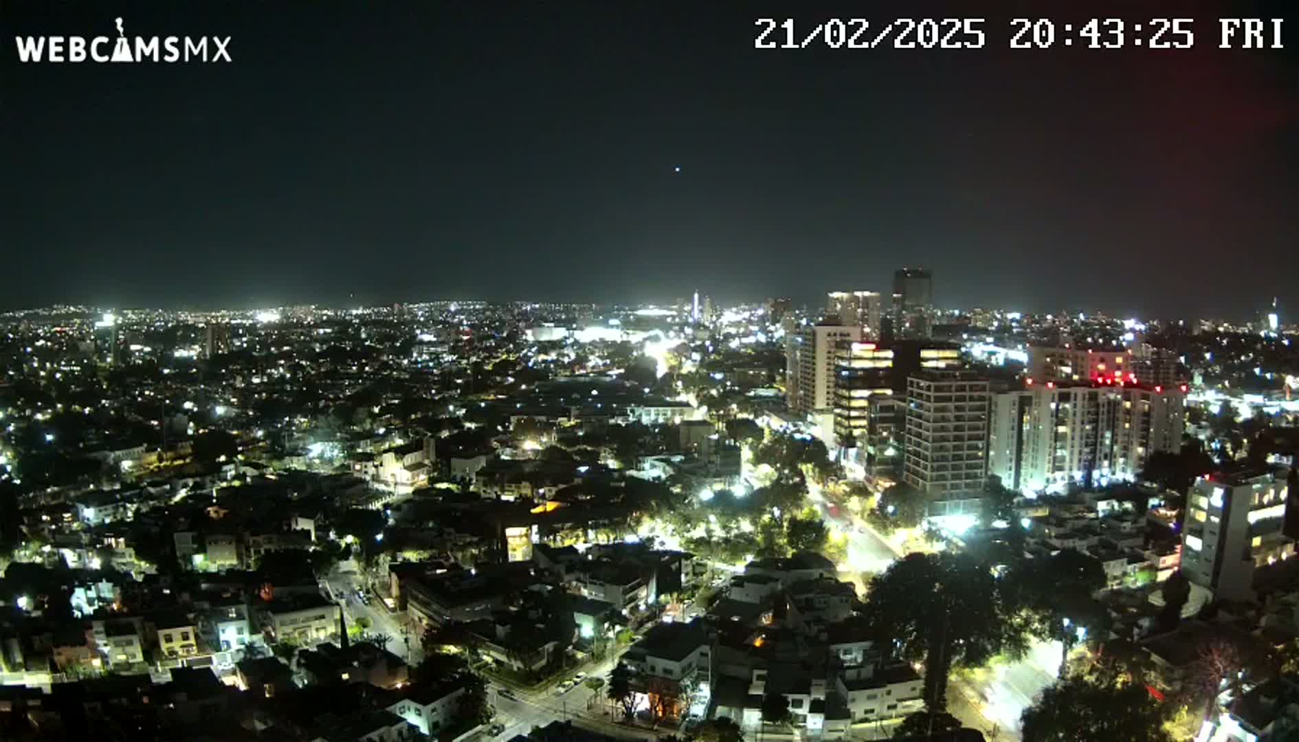 A nighttime aerial view of a sprawling city illuminated by streetlights and building lights under a clear, dark sky.