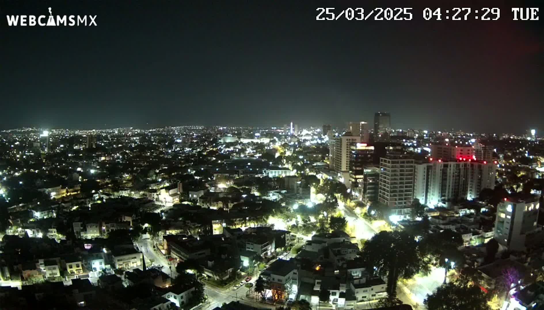 A nighttime aerial view of a city illuminated by streetlights and building lights under a clear sky.
