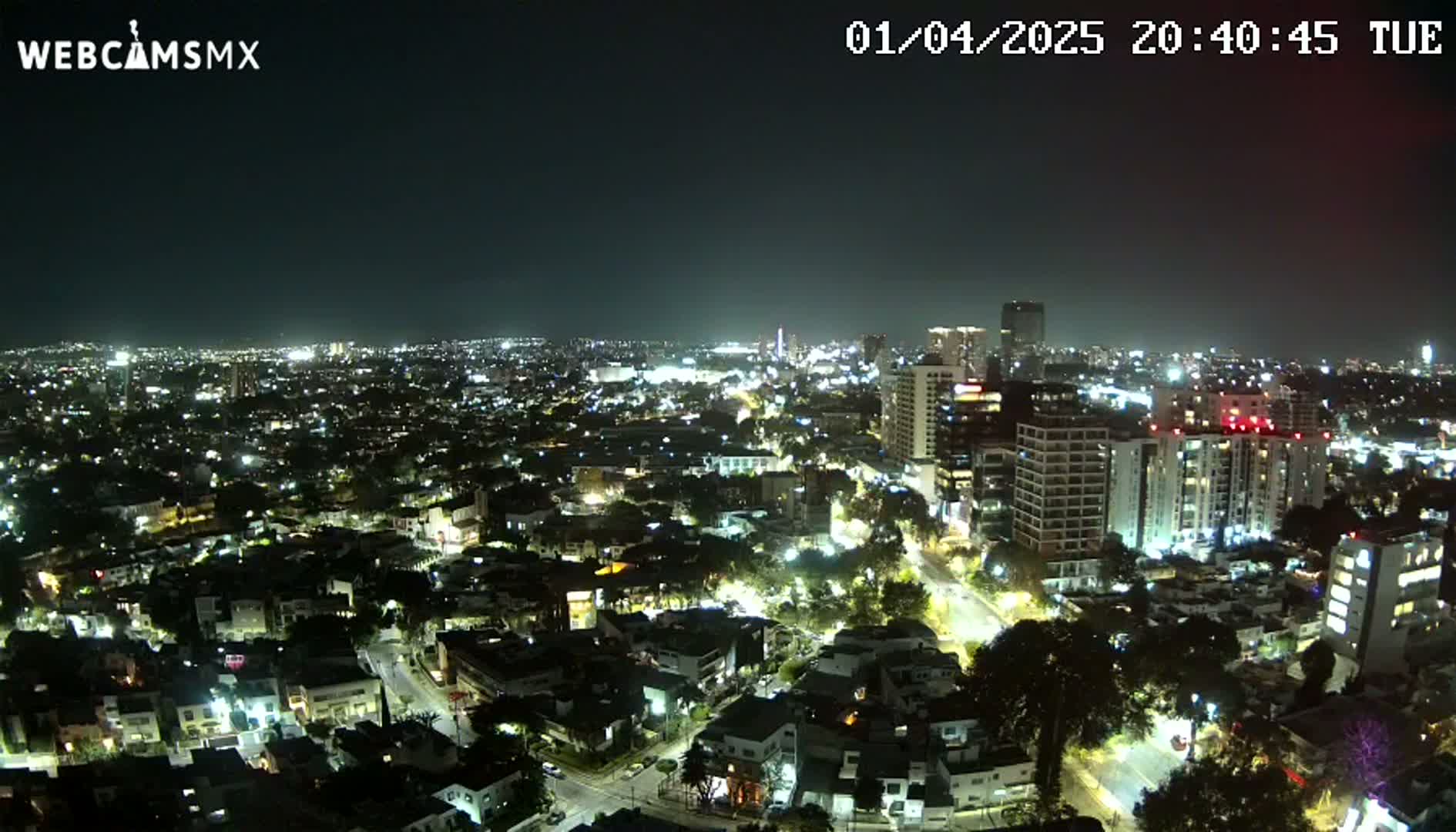 A nighttime, aerial view of a sprawling city with brightly lit buildings and streets under a clear sky.