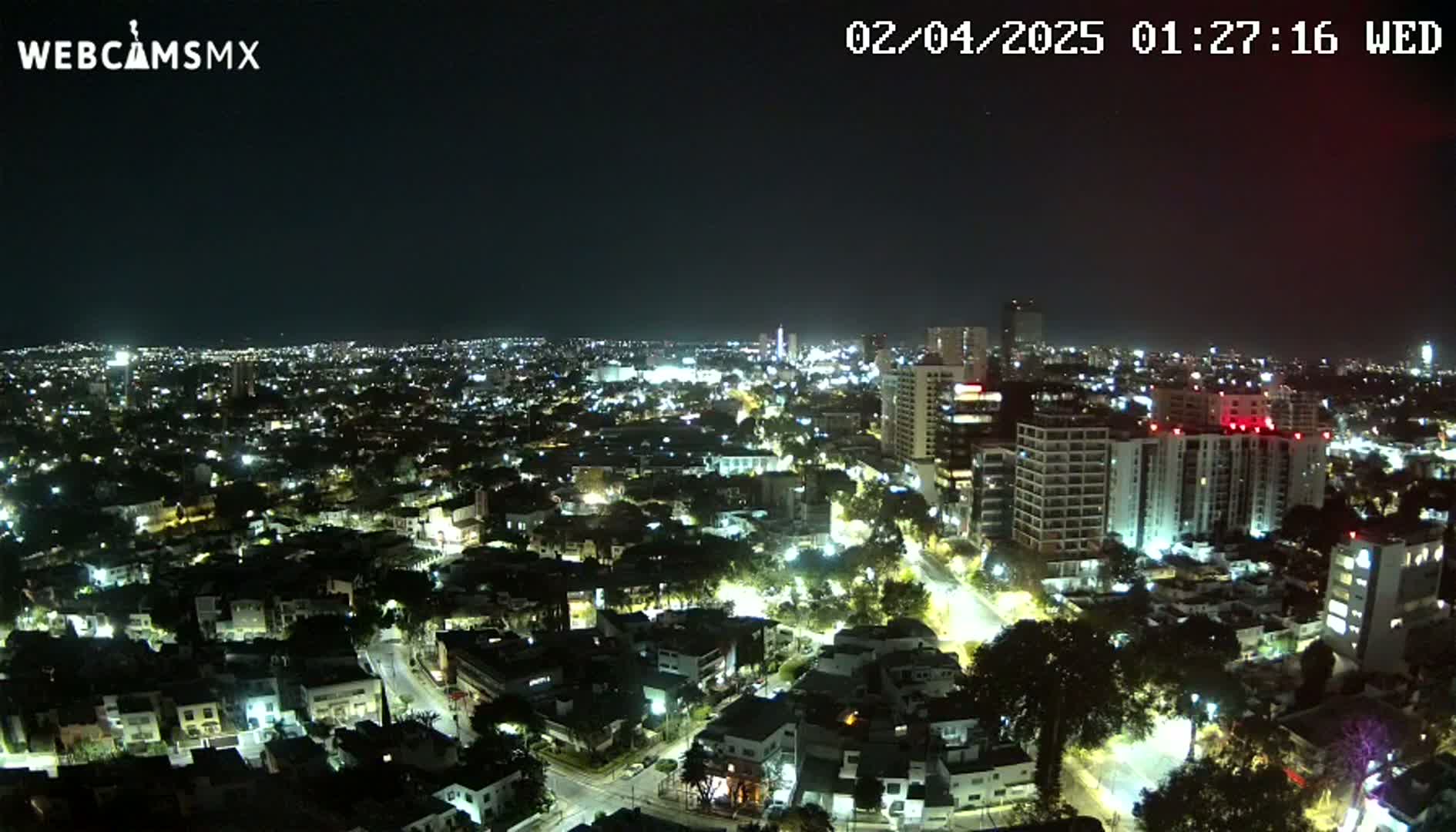 A nighttime aerial view of a city with numerous buildings illuminated, under a clear, dark sky.