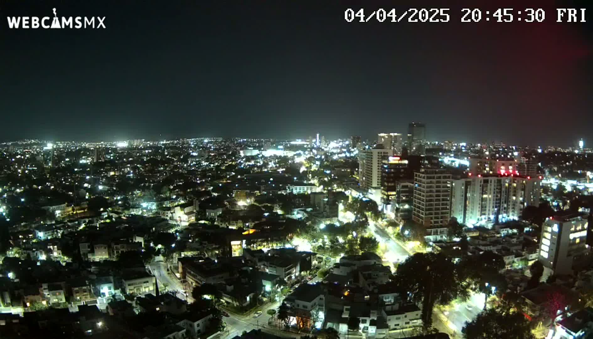 A nighttime aerial view of a city shows numerous buildings illuminated by streetlights and other lights.