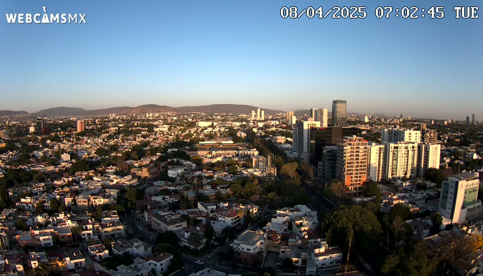 An aerial view of a city sprawling across a valley, under a clear, sunny sky at sunrise.