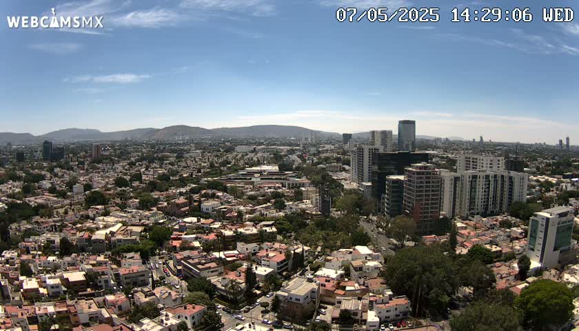 A sprawling city landscape under a clear blue sky, with mountains visible in the distance.