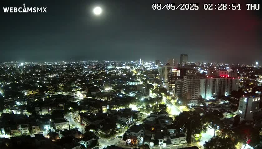 A brightly lit city is seen at night under a full moon and clear skies.