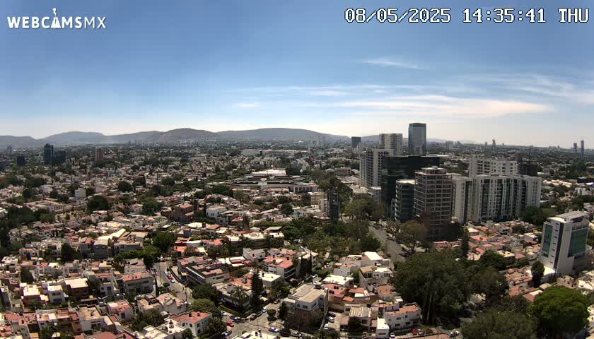 A sprawling city landscape under a clear blue sky stretches to distant mountains.