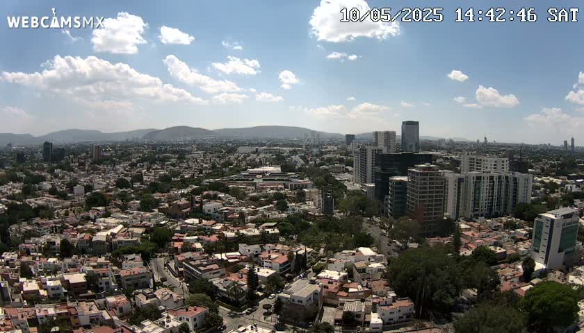 A partly cloudy daytime aerial view of a sprawling city with numerous buildings, including high-rises, and mountains in the background.