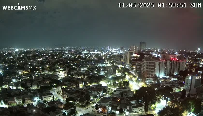 A nighttime, high-angle view of a city illuminated by streetlights under a mostly cloudy sky.