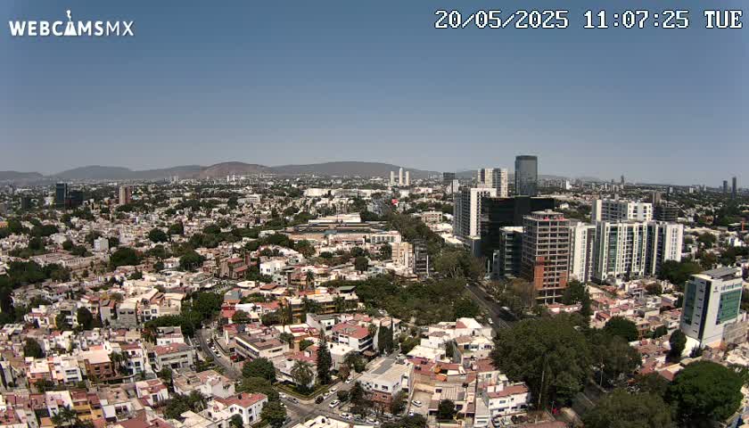A sprawling city landscape under a clear, sunny sky, showing a mix of residential buildings and high-rises.