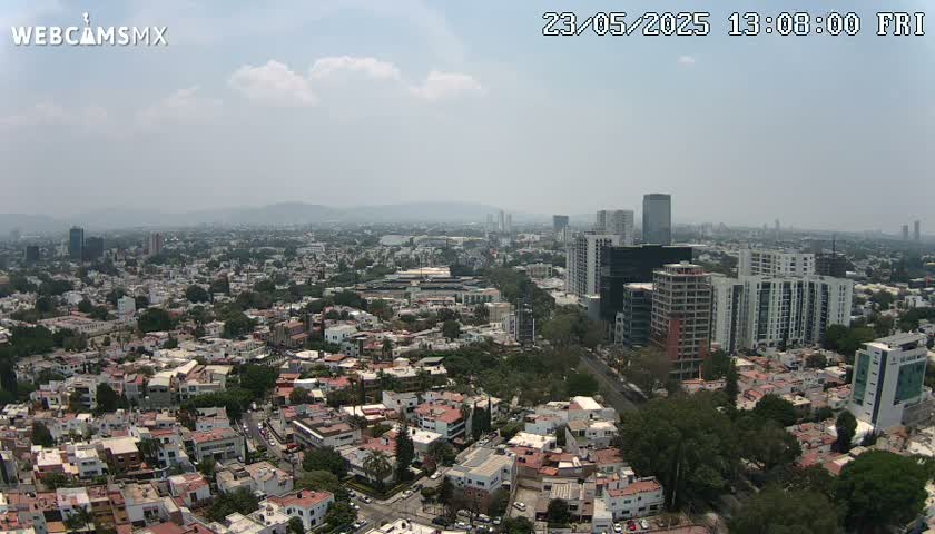 An aerial view of a sprawling city on a hazy day shows numerous buildings, from low-rise residential homes to high-rise structures, extending to the horizon.