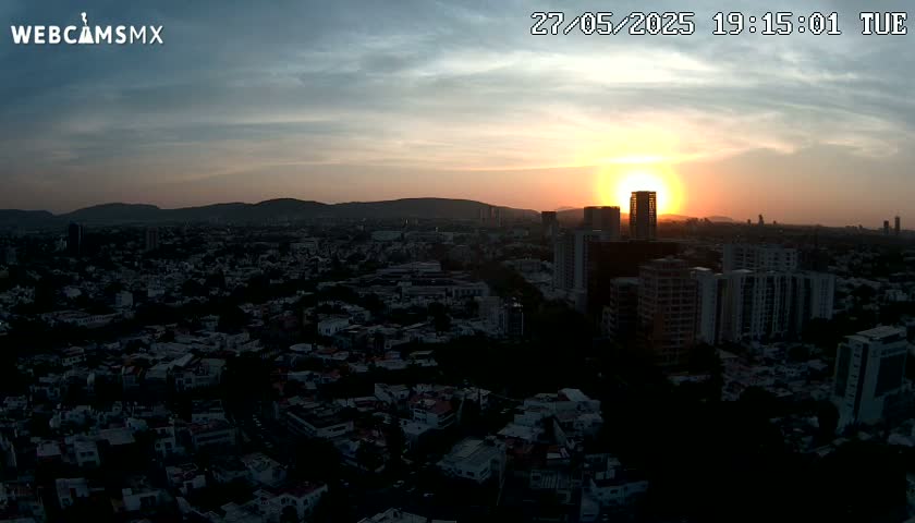 A sunset over a sprawling city, casting long shadows on the buildings below, with a mostly clear sky.