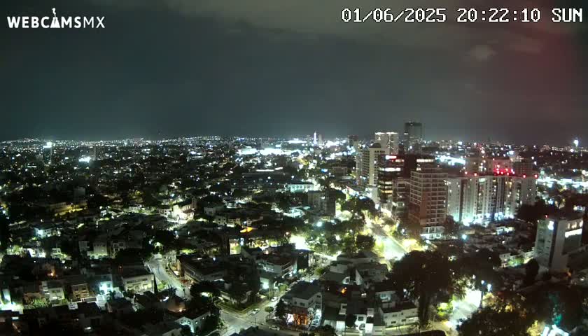 A nighttime aerial view of a city illuminated by streetlights and building lights under a partly cloudy sky.