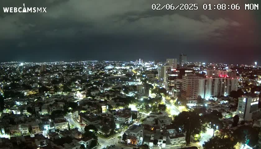 A nighttime aerial view of a city illuminated by streetlights under a dark, cloudy sky.