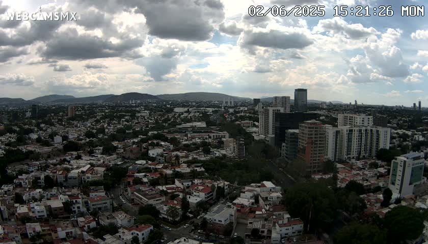 A sprawling city with many low and high-rise buildings extends to distant mountains under a partly cloudy sky.