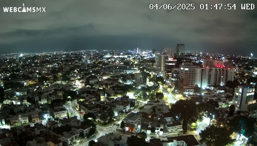 A nighttime aerial view of a city illuminated by streetlights and building lights under a cloudy sky.