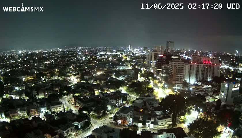 A nighttime aerial view of a city with illuminated buildings and streets under a clear, dark sky.