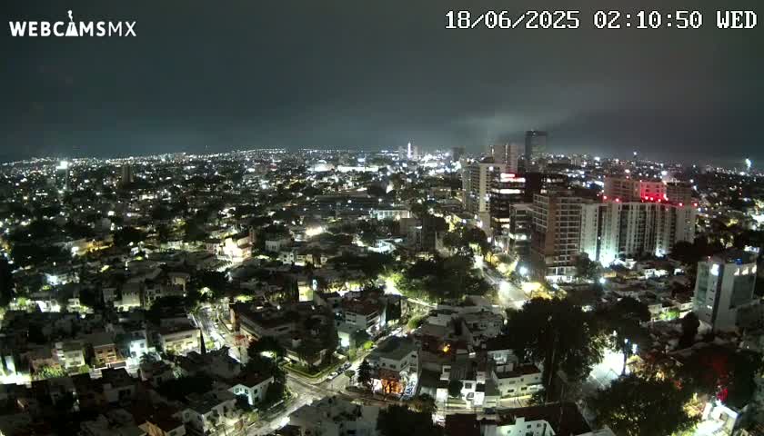 A nighttime aerial view of a city illuminated by streetlights and building lights under a mostly clear, dark sky.