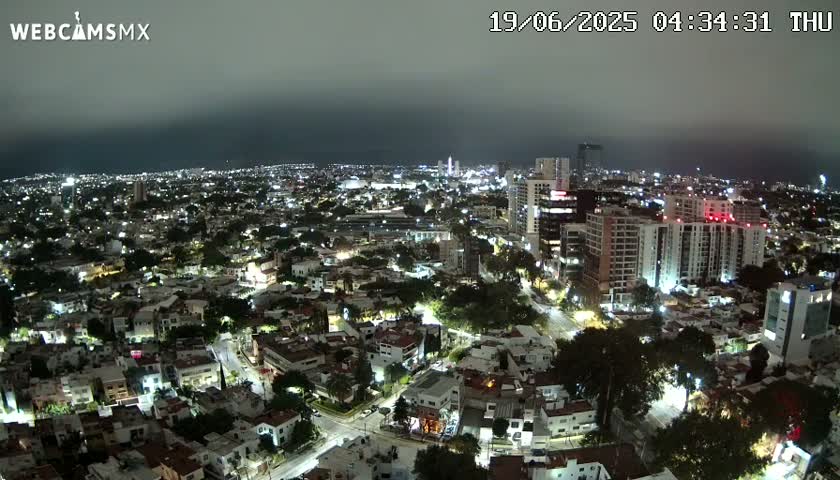 An aerial nighttime view of a city under a cloudy sky shows many illuminated buildings and roads.