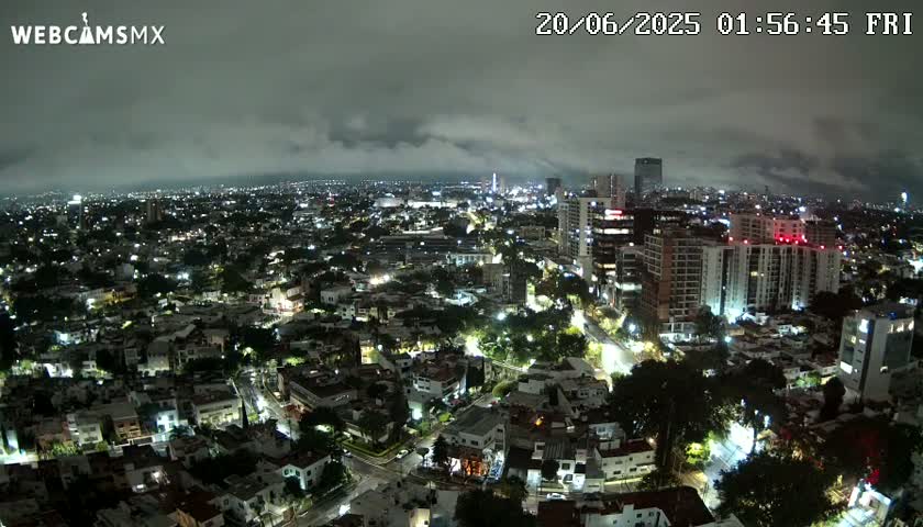 A nighttime aerial view of a city under a cloudy sky shows numerous buildings illuminated with streetlights.