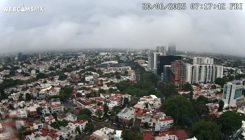 A high-angle view of a sprawling city under an overcast sky shows many residential buildings and taller structures, with some construction visible.