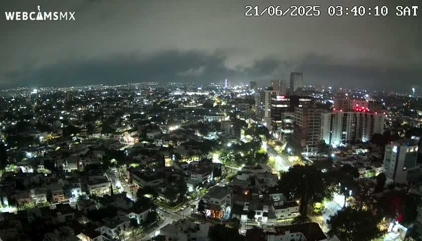 A nighttime aerial view of a city illuminated by streetlights under a cloudy sky.