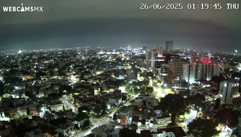 A nighttime aerial view of a city illuminated with streetlights under a dark, cloudy sky.