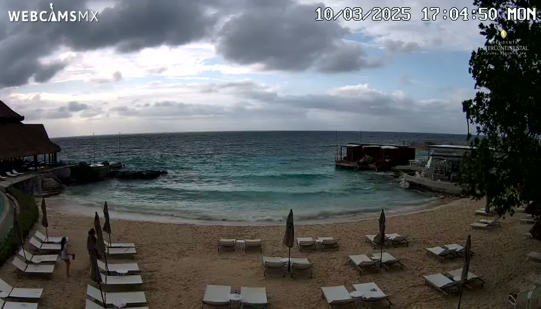 A sandy beach with lounge chairs and umbrellas, situated next to a calm ocean under an overcast sky.