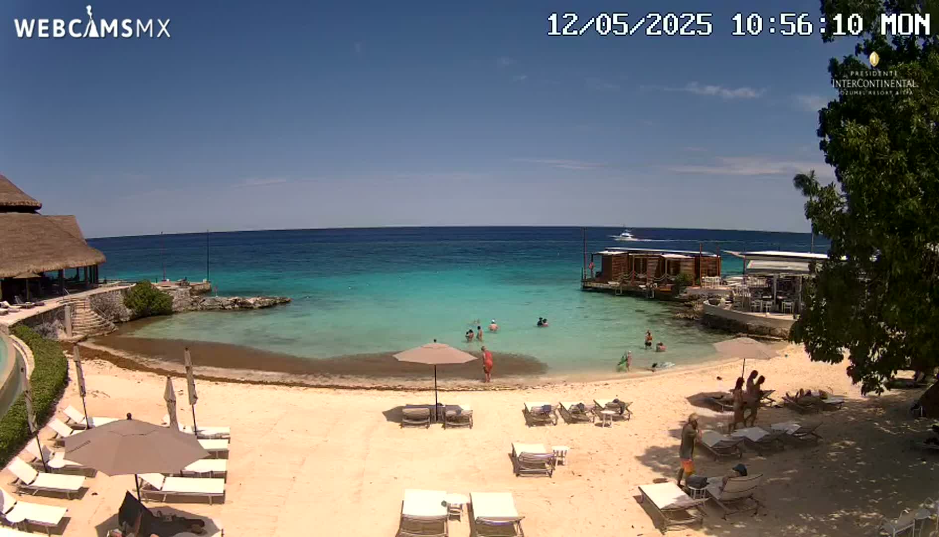 A sandy beach with lounge chairs and umbrellas sits beside a calm, turquoise ocean under a clear, sunny sky.
