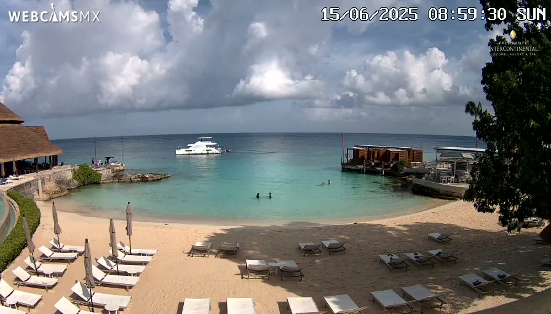 A partly cloudy sunny day at a beach resort with turquoise water, a sandy beach lined with lounge chairs, and a boat in the distance.