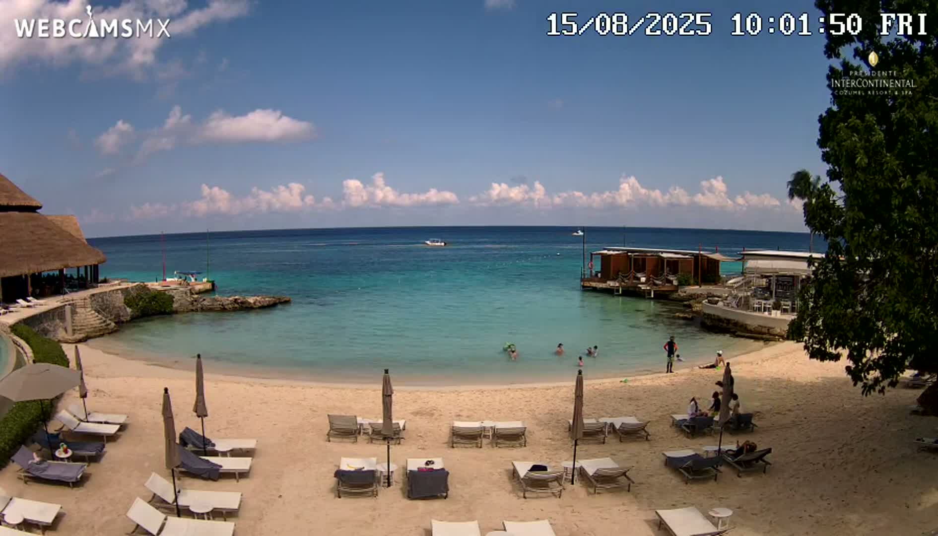 A sandy beach with lounge chairs and umbrellas, calm turquoise water with people swimming, and a partly sunny sky.