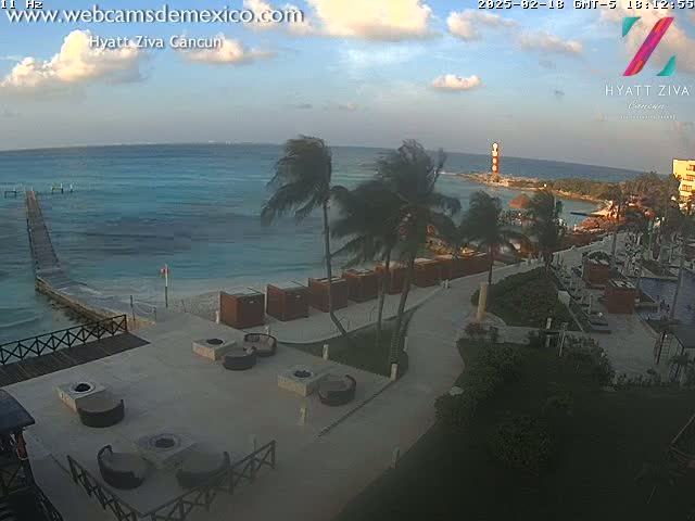 A beach resort with palm trees, a calm ocean, and partly cloudy skies.