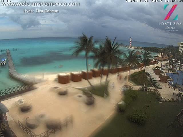 A beach resort with palm trees and turquoise water under a partly cloudy sky.