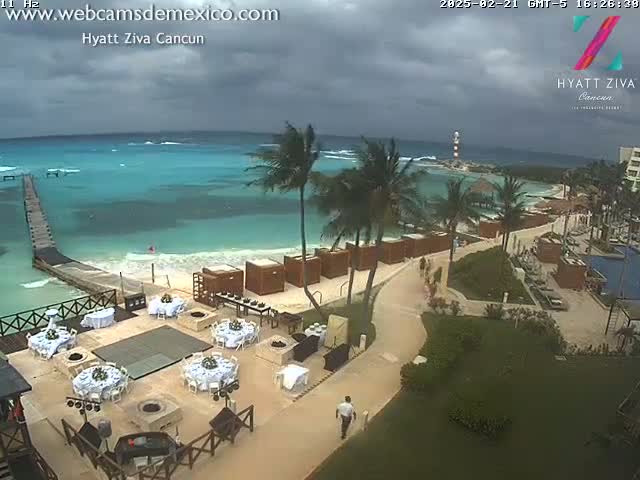 An outdoor wedding reception is taking place on a beachside resort under overcast skies, with turquoise water visible in the background.