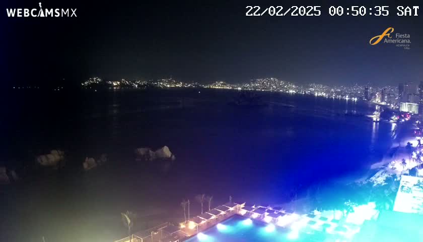 A nighttime view of a city skyline across a dark body of water, with a brightly lit pool and surrounding area in the foreground.