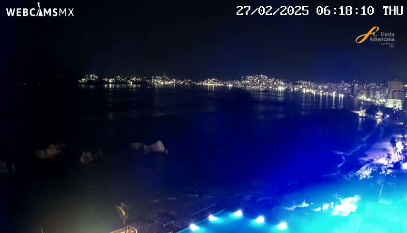 A nighttime view of a city skyline across a dark body of water, with a brightly lit pool in the foreground.