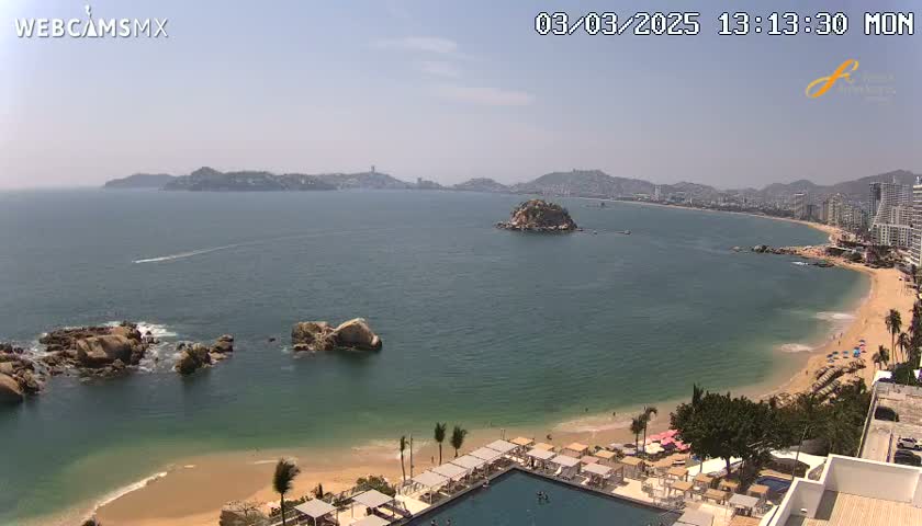 A sunny day overlooking a bay with a sandy beach, calm water, and a resort with a pool.