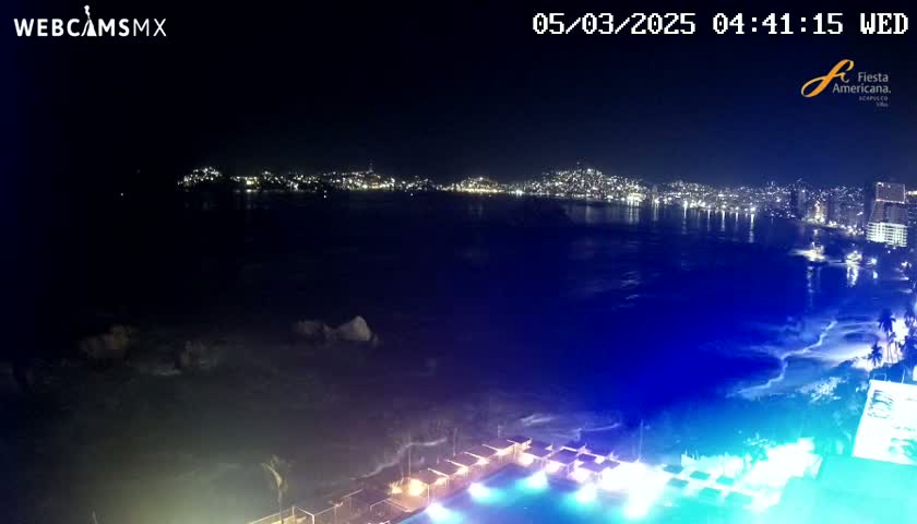 A nighttime view of a city skyline across a dark ocean, with a brightly lit pool and surrounding structures in the foreground.