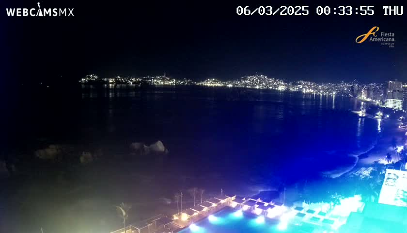 A nighttime view of a city skyline across a dark, calm ocean, with a brightly lit pool and surrounding structures in the foreground.