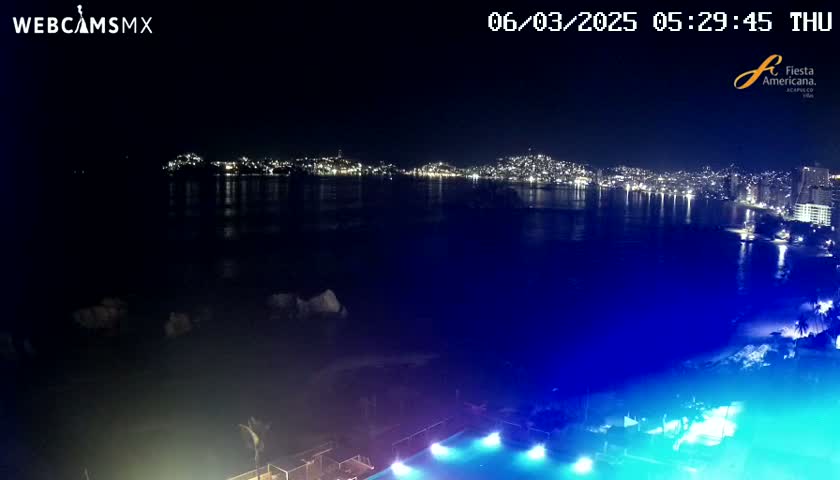 A nighttime view of a city skyline across a dark body of water, with a brightly lit swimming pool in the foreground.