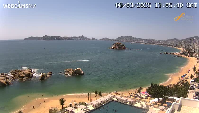 A sunny beach with clear turquoise water and a distant city skyline is visible from a high vantage point.