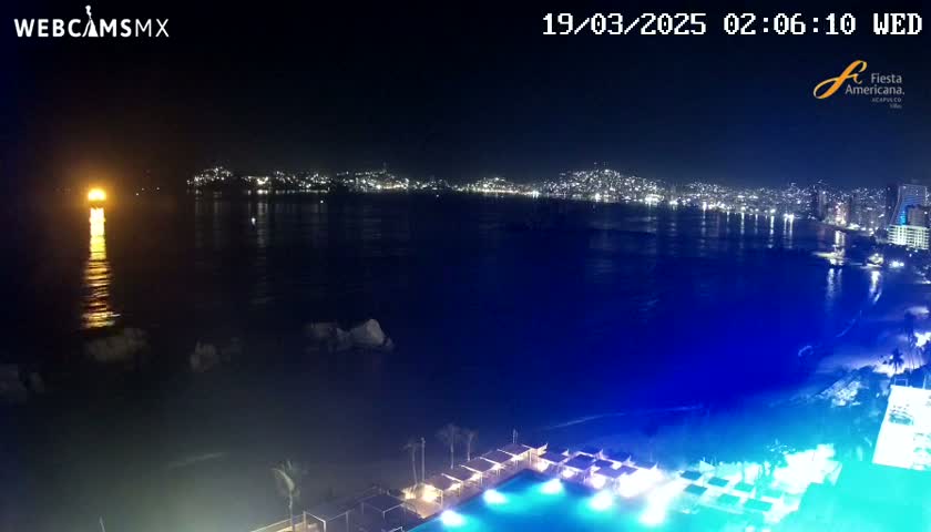 A nighttime view of a city skyline across a dark blue body of water, with a brightly lit swimming pool and surrounding structures in the foreground.