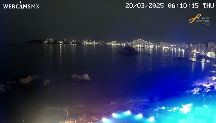 A nighttime view of a city's lights reflected on a calm body of water, with a brightly lit pool in the foreground.