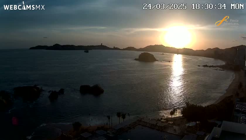 A sunset over a calm bay with rocky outcrops and a beach, viewed from an elevated position.