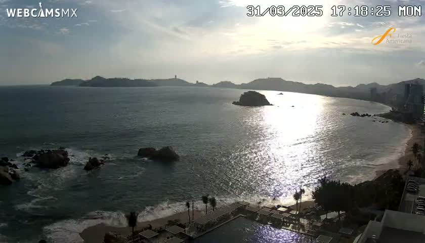 A partly cloudy sunset over a calm ocean with a beach and resort visible in the foreground.