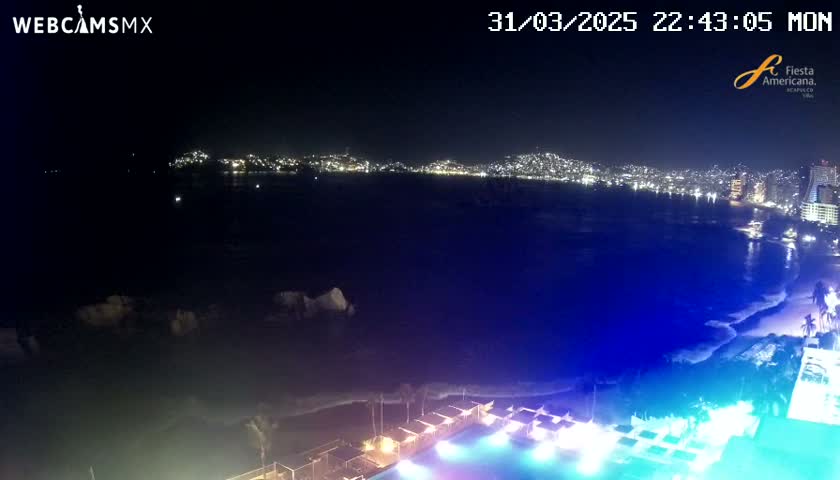 A nighttime view of a city's illuminated coastline across a dark body of water, with a brightly lit pool and surrounding structures in the foreground.
