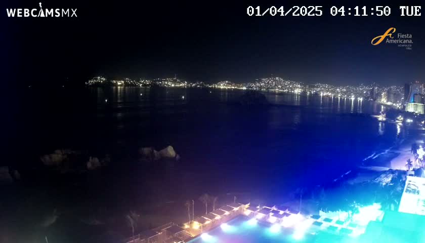 A nighttime view of a city skyline across a dark body of water, with a brightly lit pool and surrounding structures in the foreground under a clear sky.