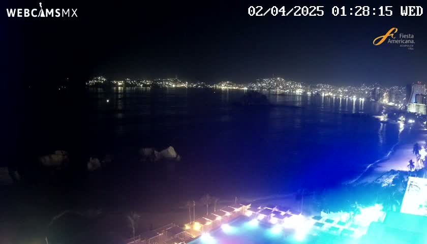 A nighttime view of a city across a dark bay, illuminated by lights along the shoreline and on the water, with a brightly lit pool area in the foreground.