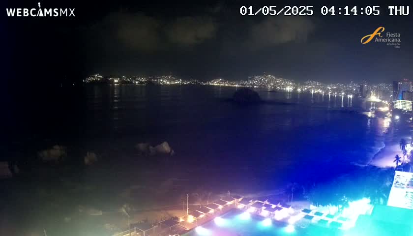 A nighttime view of a city skyline across a dark body of water, with a brightly lit pool and surrounding structures in the foreground under a partly cloudy sky.