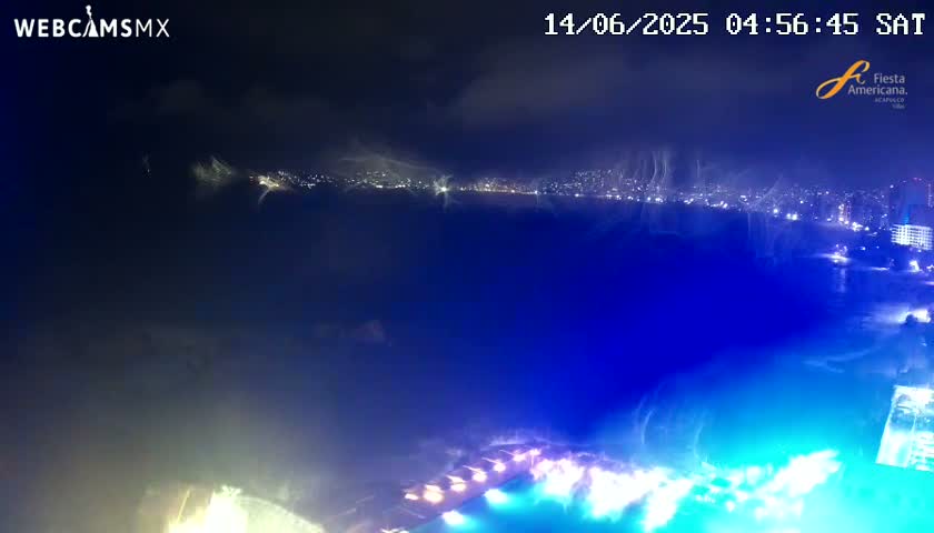 A nighttime view of a city skyline across a body of water, partially obscured by hazy clouds or fog.