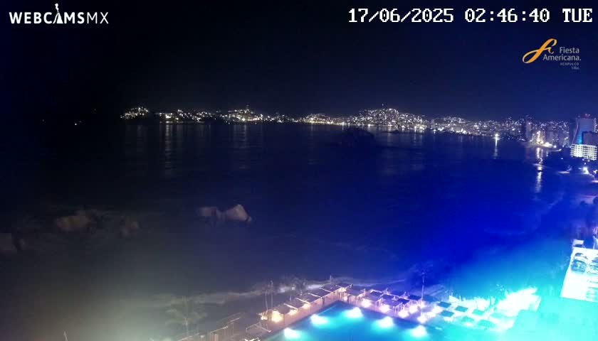 A nighttime view of a city skyline across a dark ocean, with a brightly lit swimming pool and surrounding structures in the foreground.