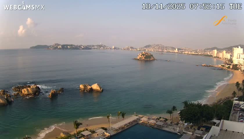 A clear night reveals a sprawling city skyline brightly illuminating a wide bay, with its lights reflecting on the dark water and a vibrantly lit resort pool visible in the foreground.